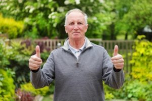 mesothelioma survivor with thumbs up in front of garden